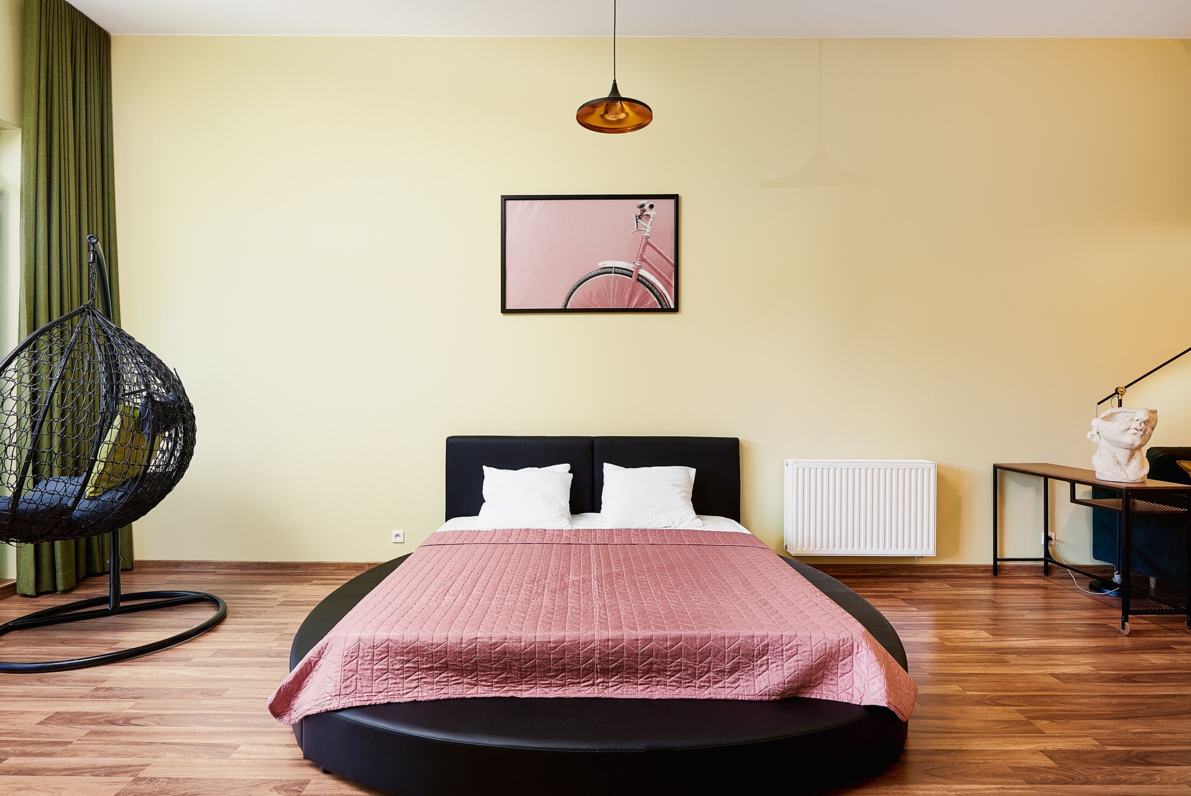 A bedroom with a bed, a hanging chair, a radiator, and a framed picture on the wall.