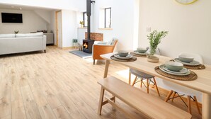 A modern living room with a fireplace, a dining area with a wooden table and benches, and a sofa.