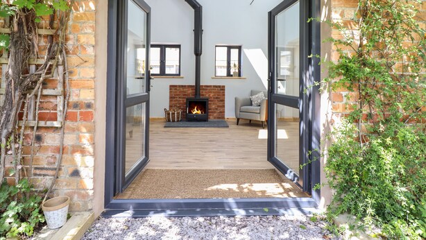 An open doorway leading to a living room with a brick fireplace, a sofa, and a chair.