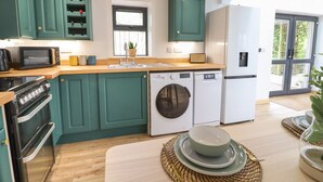 A modern kitchen with teal cabinets, a microwave, stove, washing machine, and refrigerator.