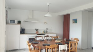 Une cuisine moderne avec des meubles blancs, un four à micro-ondes encastré et une machine à café. On y trouve une table à manger avec des chaises et un luminaire suspendu au-dessus.