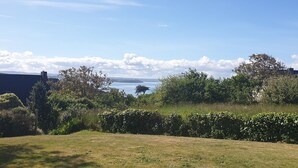 Une zone herbeuse offrant une vue sur une étendue d’eau et sur des collines lointaines.