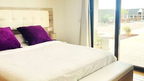 Ein modernes Schlafzimmer mit einem großen Bett, zwei violetten Kissen und einem Holz-Kopfteil.