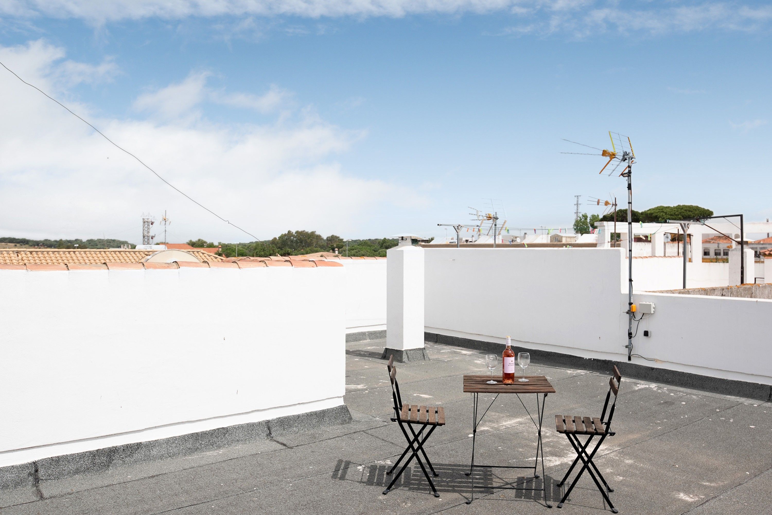 Una terraza en la azotea con una mesa, sillas, una botella de vino y una antena.