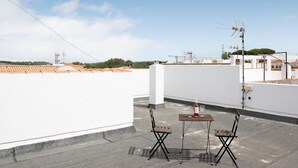 Une terrasse sur le toit avec une table et des chaises, une bouteille de vin et une antenne.