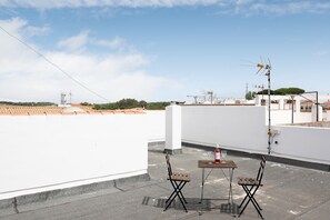 Een terras op het dak met een tafel, stoelen, een fles wijn en een antenne.