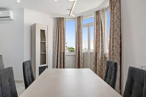 A conference room with a long table, grey chairs, patterned curtains, a white door, and a view of buildings through the window.
