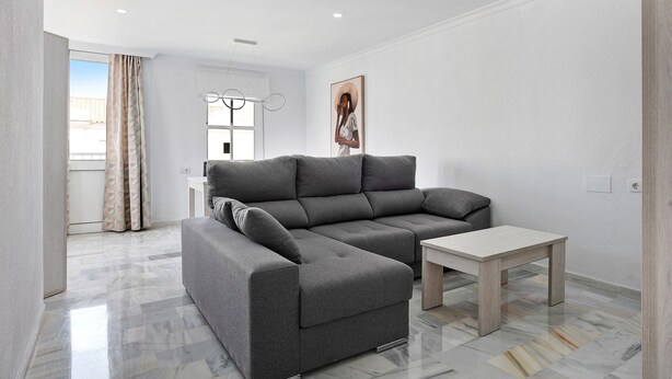 Un salon moderne avec un canapé d’angle gris, une petite table basse en bois et un tableau accroché au mur.