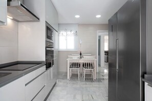 A modern kitchen with a dining area, featuring a built-in oven, a refrigerator, and a wall-mounted phone.