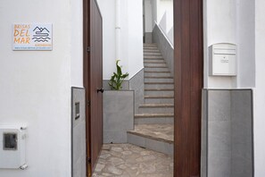 A narrow stairway leading to a wooden door, with a sign on the wall and a small plant by the steps.