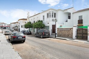 Straatbeeld met geparkeerde auto's, een wit gebouw met balkon en een stenen muur met poort.