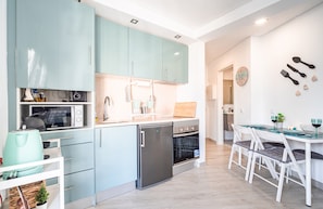 A modern kitchen with light blue cabinets, a stainless steel refrigerator, and a dining area with white chairs and a glass table.