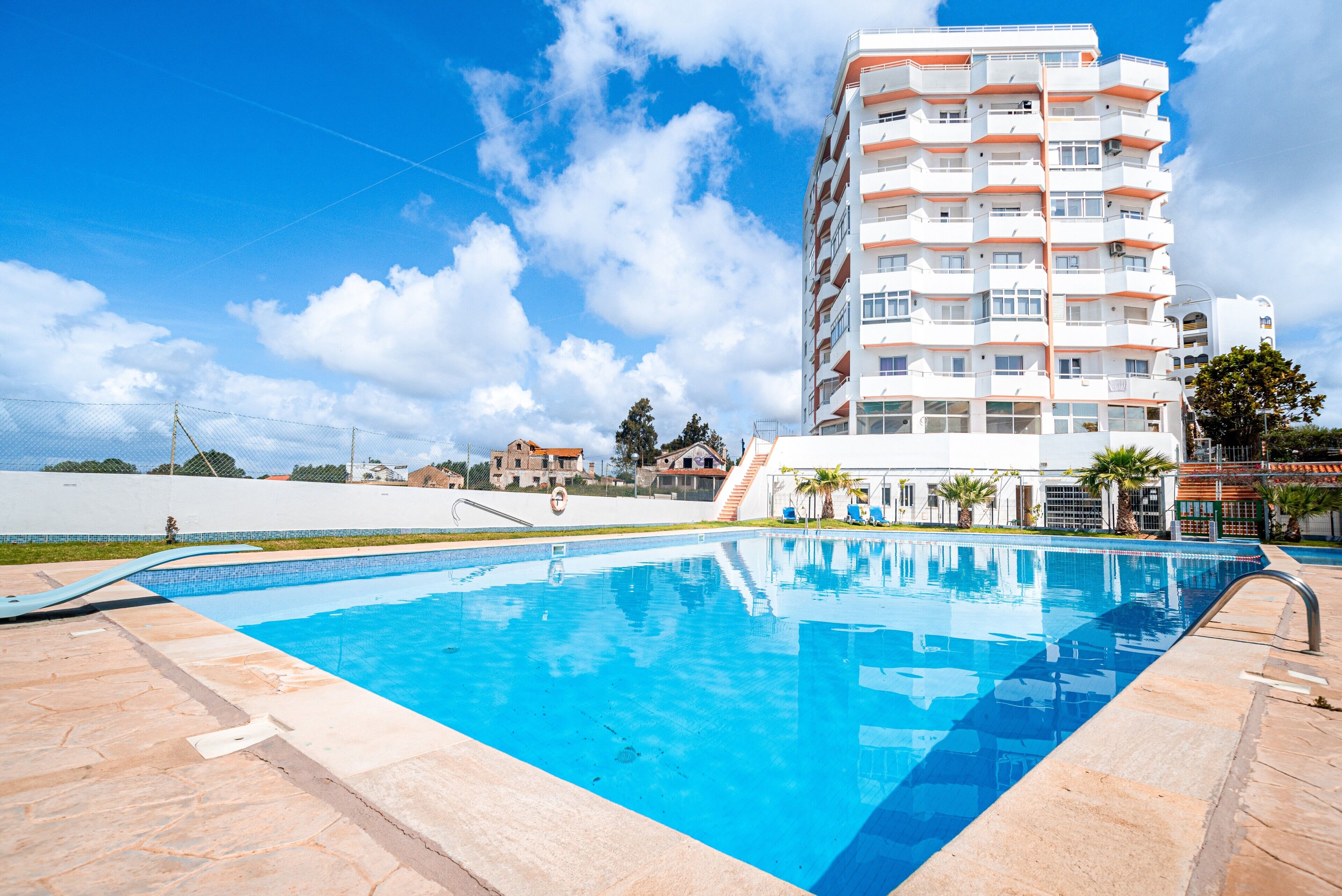 Piscina com céu azul límpido e um edifício alto ao fundo.