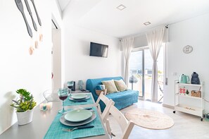 A modern living room with a dining area, a sofa, a TV, and a kitchenette.