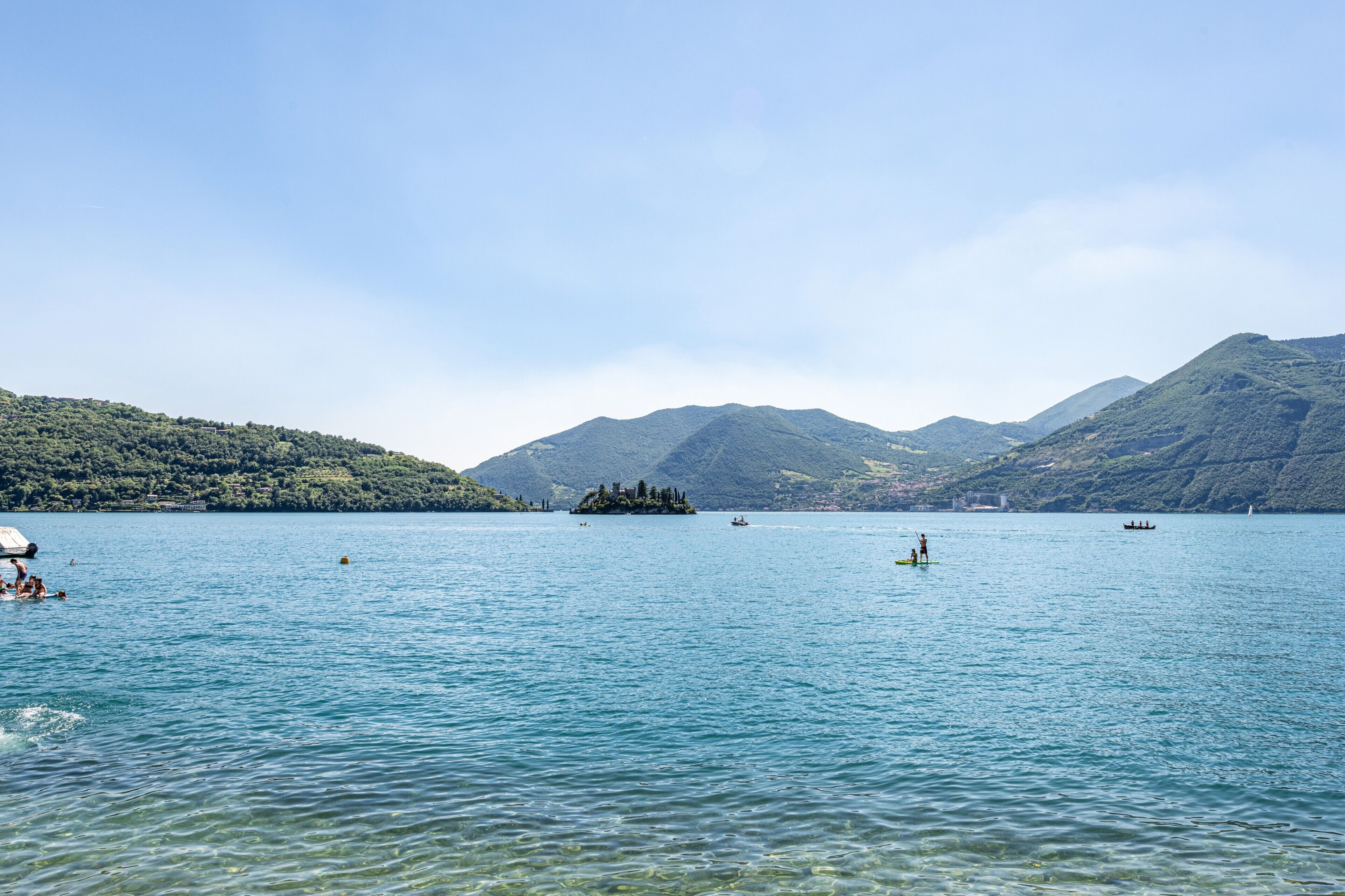 Un lago tranquilo con barcos, una pequeña isla y montañas al fondo.