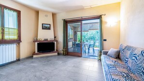 Un salon comprenant un canapé, un téléviseur à écran plat, une cheminée et une porte-fenêtre coulissante donnant sur un espace extérieur aménagé avec des chaises.