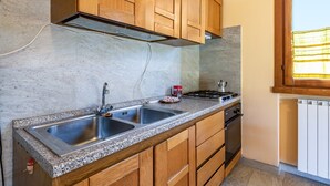 Une cuisine dotée de plans de travail en granit, d’un évier en acier inoxydable, de meubles en bois, d’une cuisinière et d’une fenêtre avec des stores.