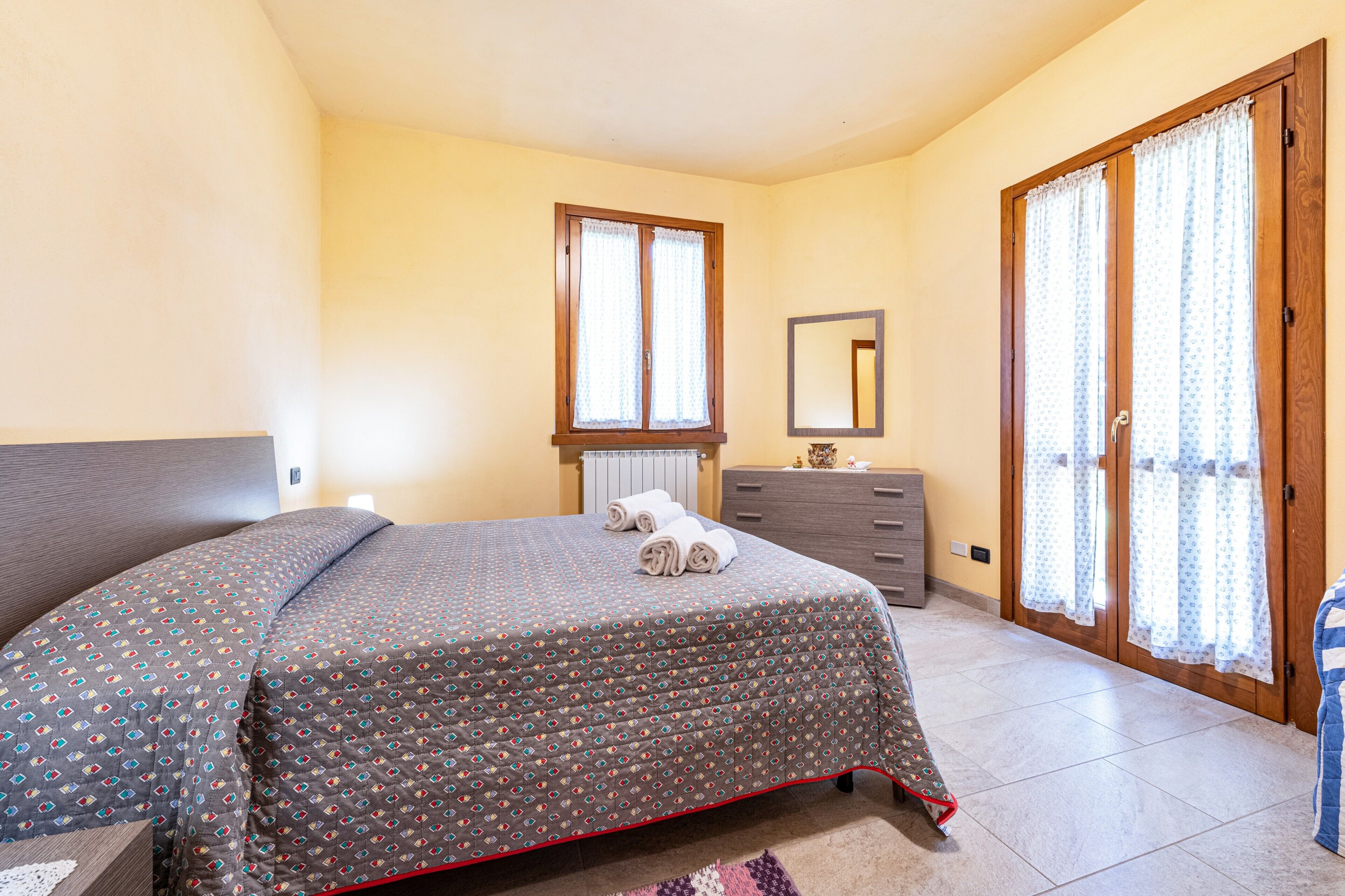 Une chambre à coucher avec un lit, une commode, un miroir et une porte avec des rideaux.