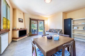 Una sala de estar con televisión, sofá, mesa de comedor y una estantería.