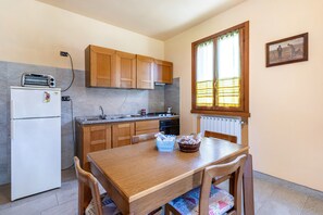 Una cocina con armarios de madera, un refrigerador blanco, un tostador, un fregadero y una ventana con cortinas.
