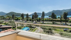 Een balkon met uitzicht op een meer, bergen en een weg met auto's.