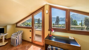 Een kamer met een bureau, stoel en grote ramen met uitzicht op een meer en bergen.