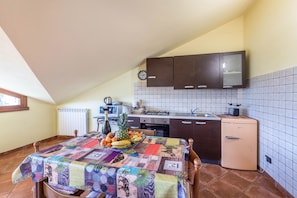 Una cocina con salpicadero de azulejos, un refrigerador y una mesa de comedor con mantel colorido.