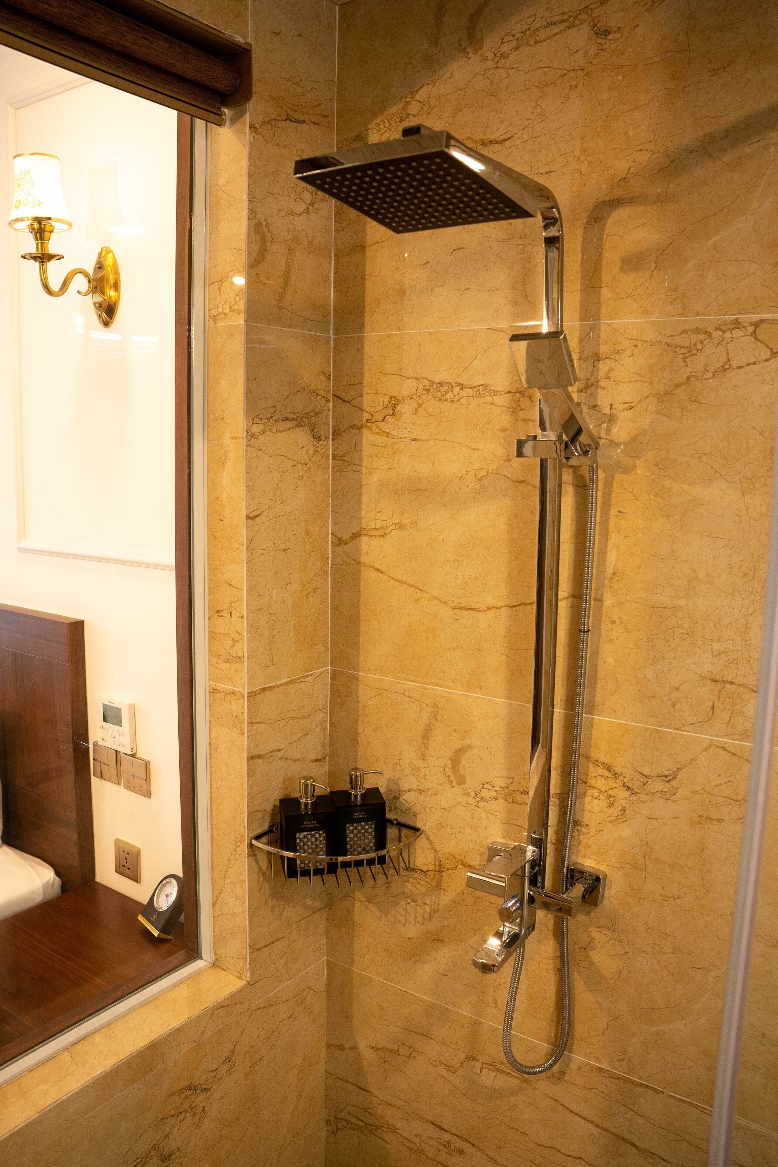 Een douche met een handdouche en een kraan op de muur, een klein plankje met toiletartikelen, en een klok aan de wand.