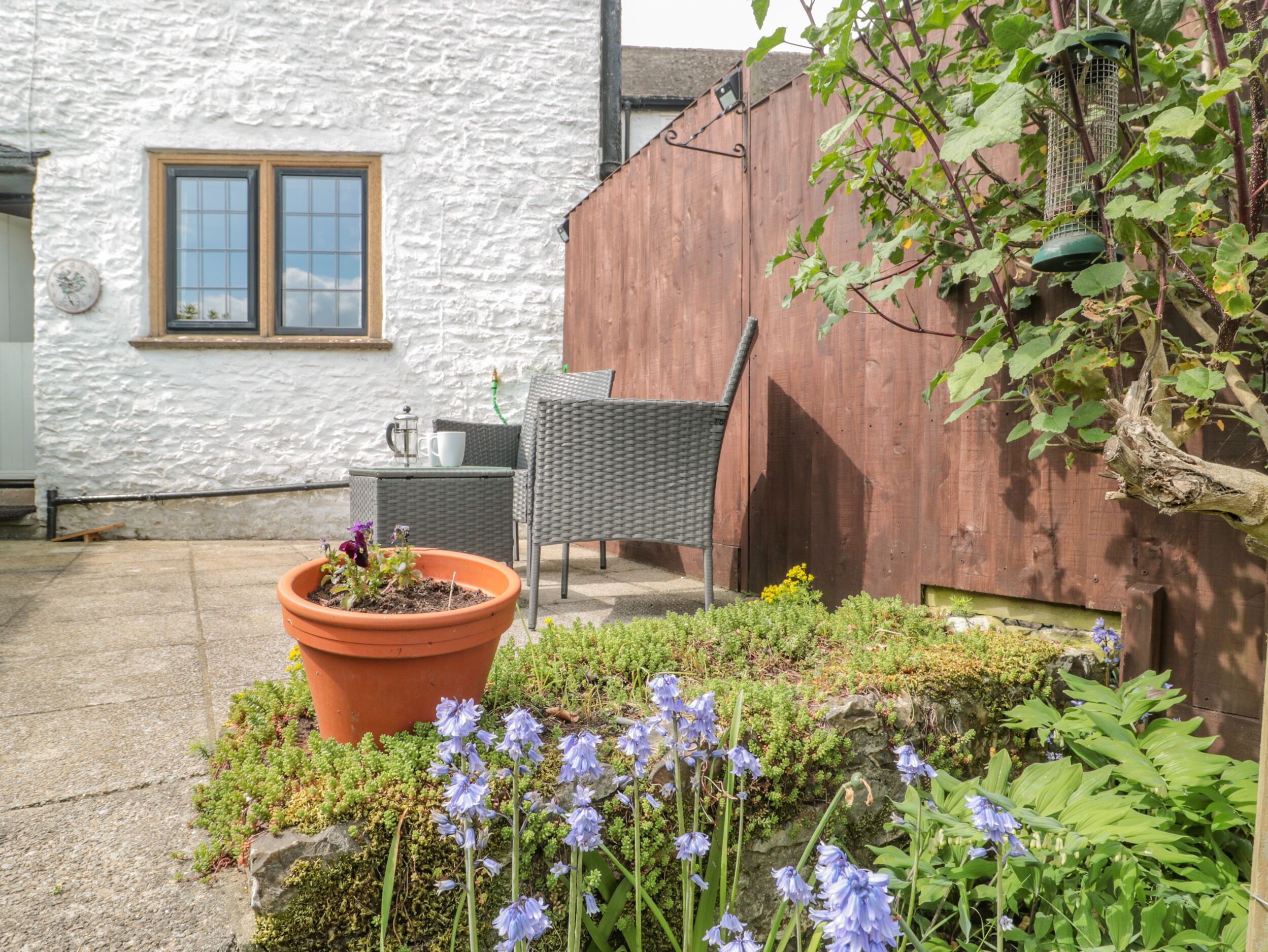A patio with a large terracotta pot, wicker furniture, and a wooden fence.