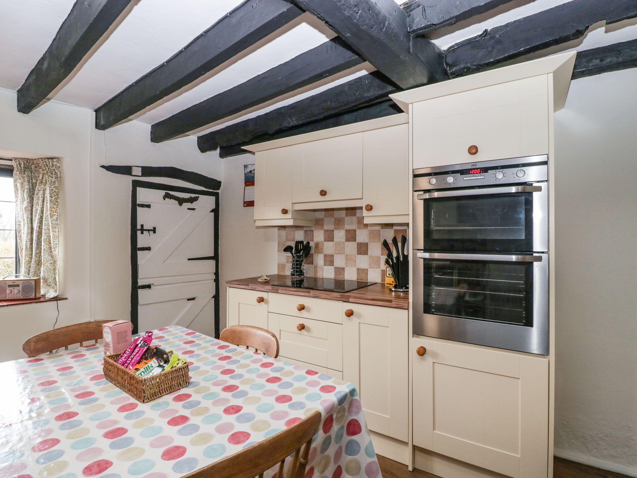 Une cuisine équipée d’une cuisinière à deux brûleurs, d’un four à micro-ondes et d’un four double. On y trouve une table recouverte d’une nappe à pois et un panier rempli d’en-cas.