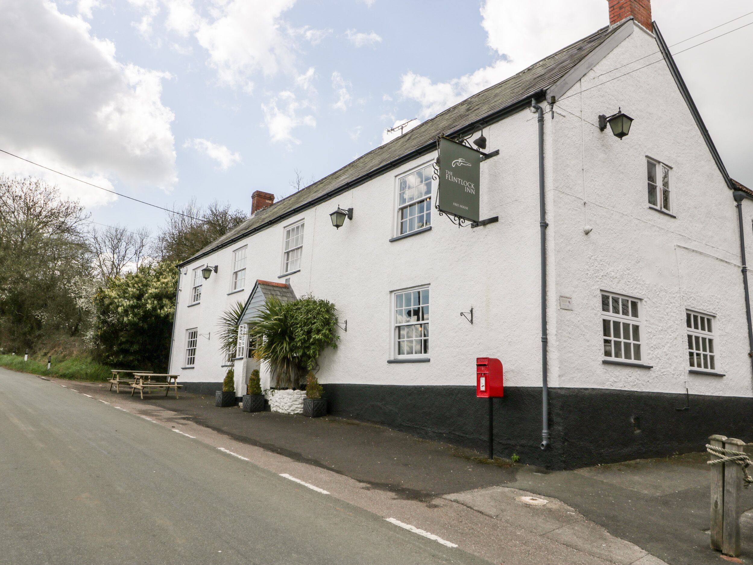Un edificio blanco con base negra, un buzón rojo y un cartel que anuncia The Fintlock Inn.