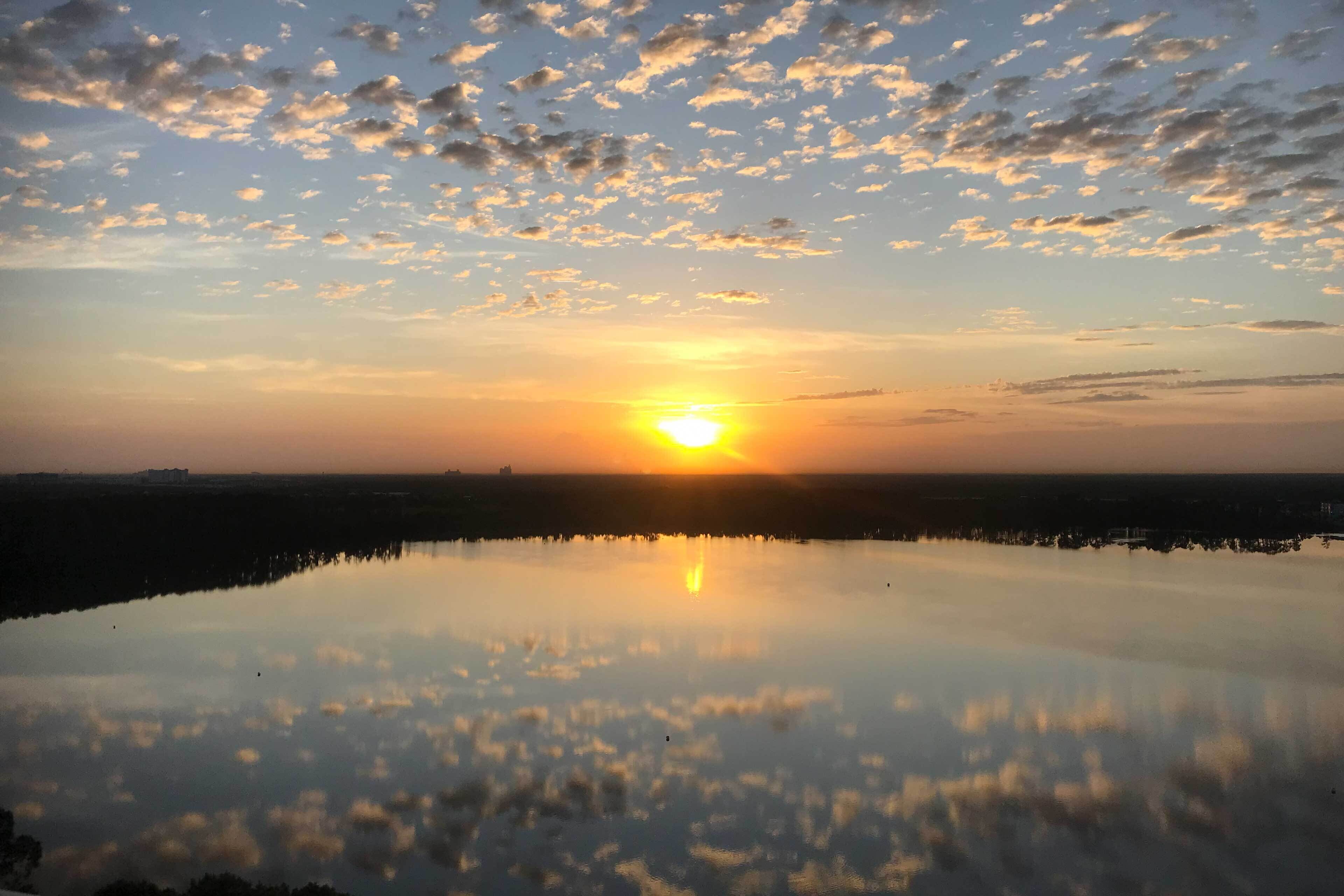 A sunset over a calm body of water with a clear reflection of the sky and clouds.