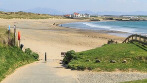 Une route côtière menant à une plage, avec un pont en bois, des zones herbeuses et des maisons en arrière-plan.