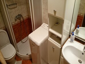 A compact bathroom with a toilet, a shower, a small washing machine, and a sink. - Apartment Nemo (Omisalj)
