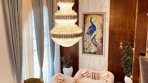 A luxurious living room with a large chandelier, plush seating, and a peacock painting on the wall.