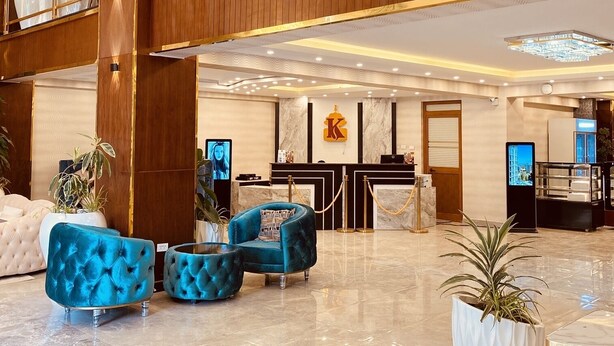 A spacious lobby with a high ceiling, a reception desk, and a seating area with blue upholstered chairs.