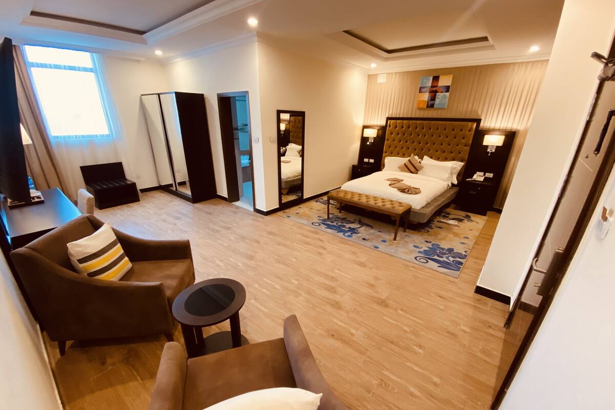A modern hotel room with a large bed, a sofa, a small table, and a mirror.