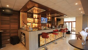 A bar area with a TV screen, bar stools, and a variety of bottles.