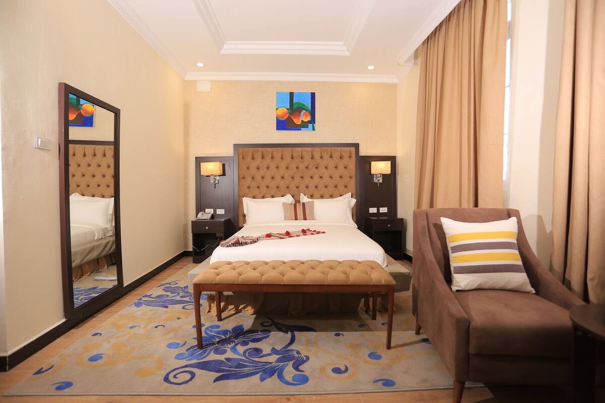 A hotel room with a large bed, a bench, a chair, a nightstand, and a mirror.