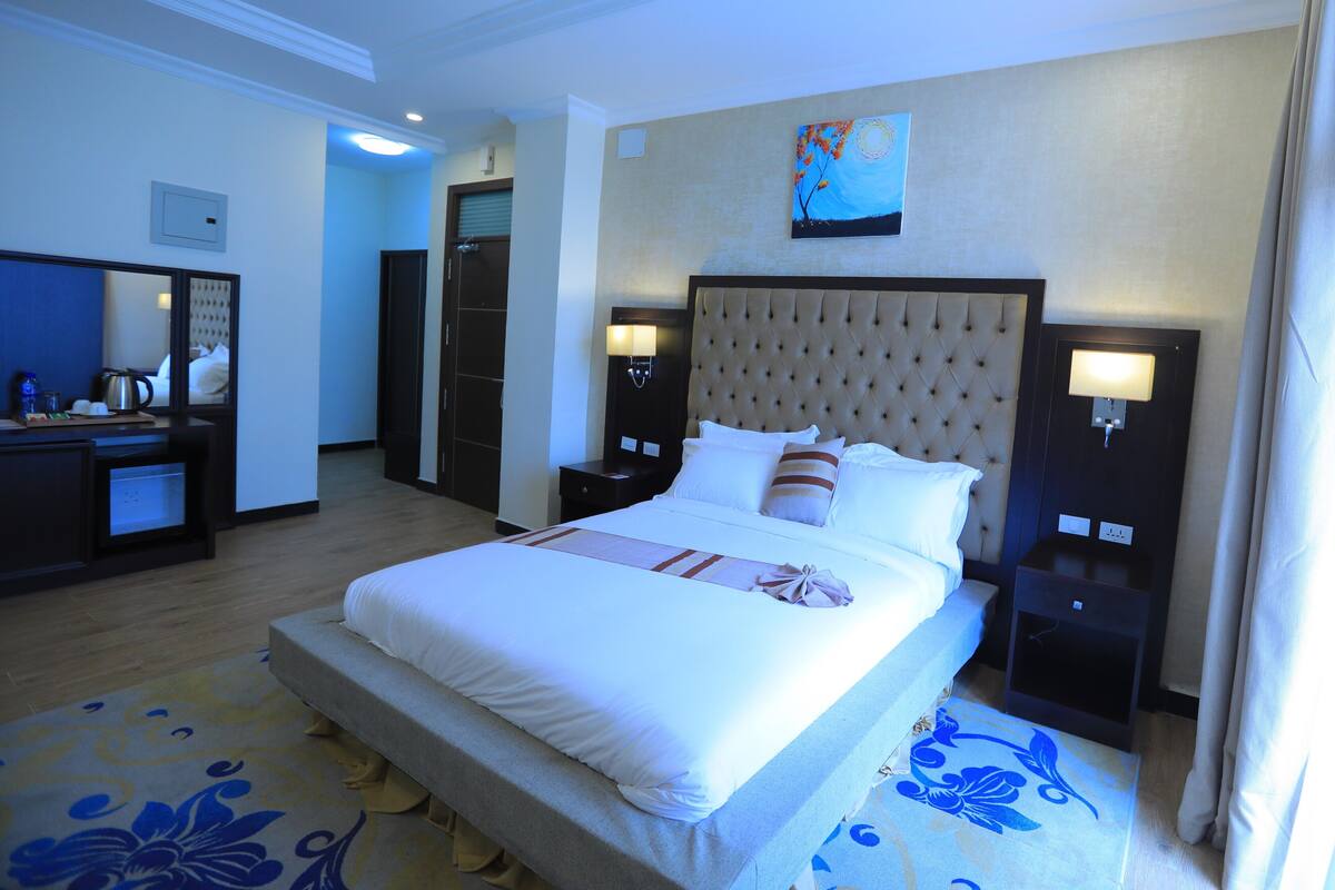 A hotel room with a large bed, a dresser, a mirror, and a painting on the wall.