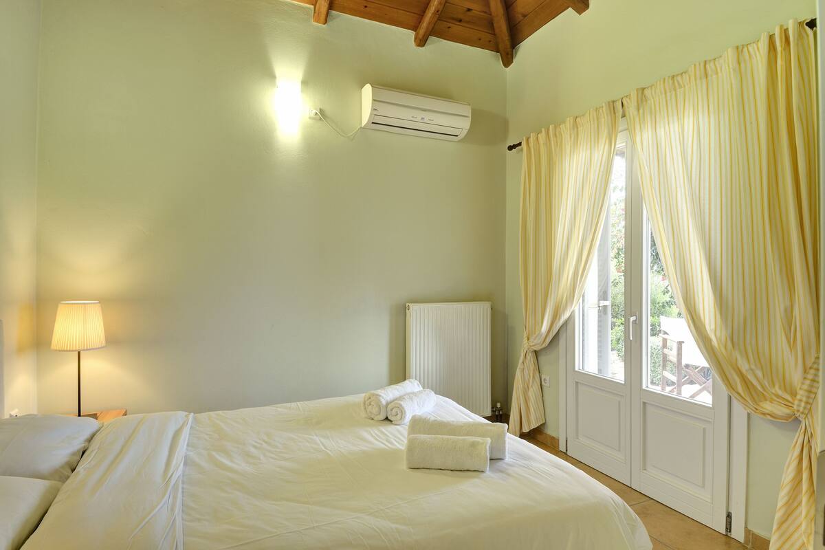 A bedroom with a bed, a radiator, a window with curtains, and a wall-mounted air conditioner.