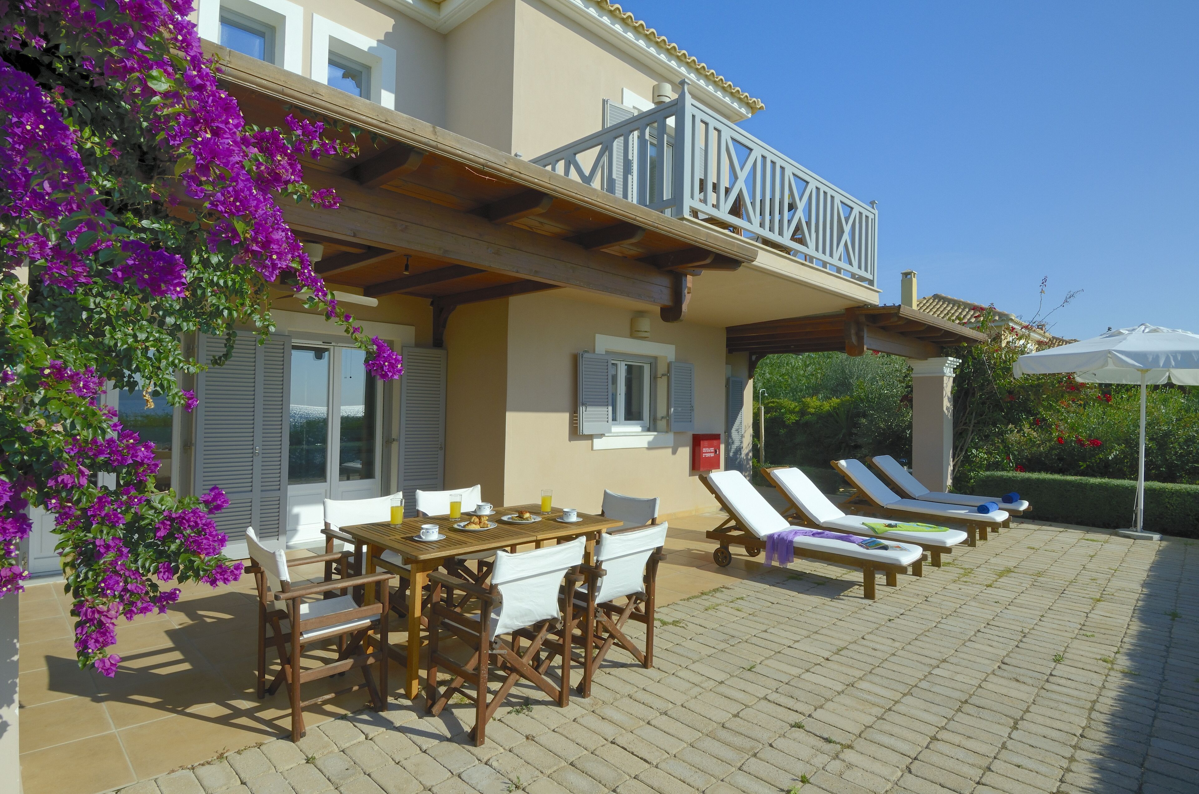 Eine Terrasse mit Tisch und Stühlen, Liegestühlen und ein Balkon mit Geländer.