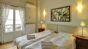 Une chambre d’hôtel comprenant un lit, deux tables de chevet, une commode, une fenêtre avec des rideaux, un appareil de climatisation et un tableau au mur.