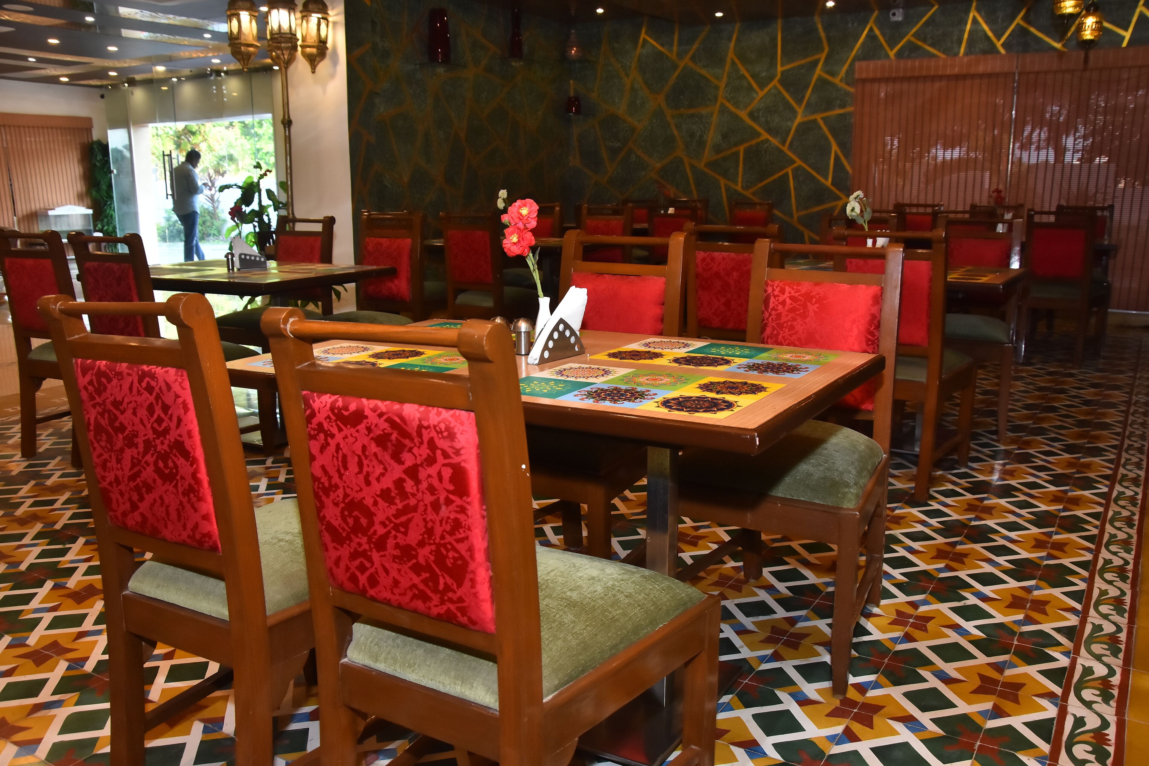 A restaurant with wooden chairs and tables, red cushions, and a patterned floor.