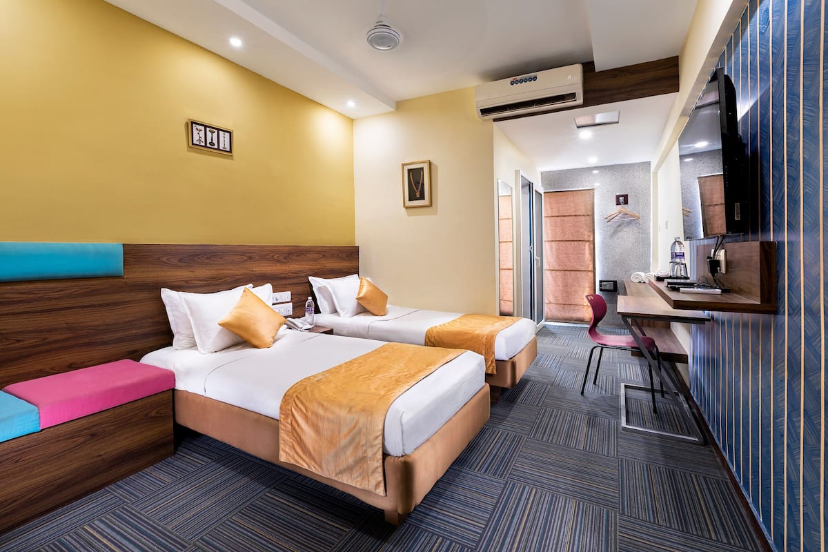 A hotel room with two beds, a desk, and a chair. There is a window, a door, and an air conditioning unit.