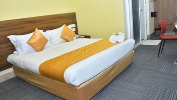 A hotel room with a bed, pillows, a blanket, and a chair.