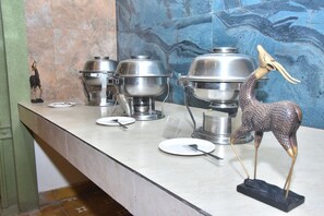 A buffet setup with multiple stainless steel chafing dishes, a decorative giraffe figurine, and a small statue of a person.