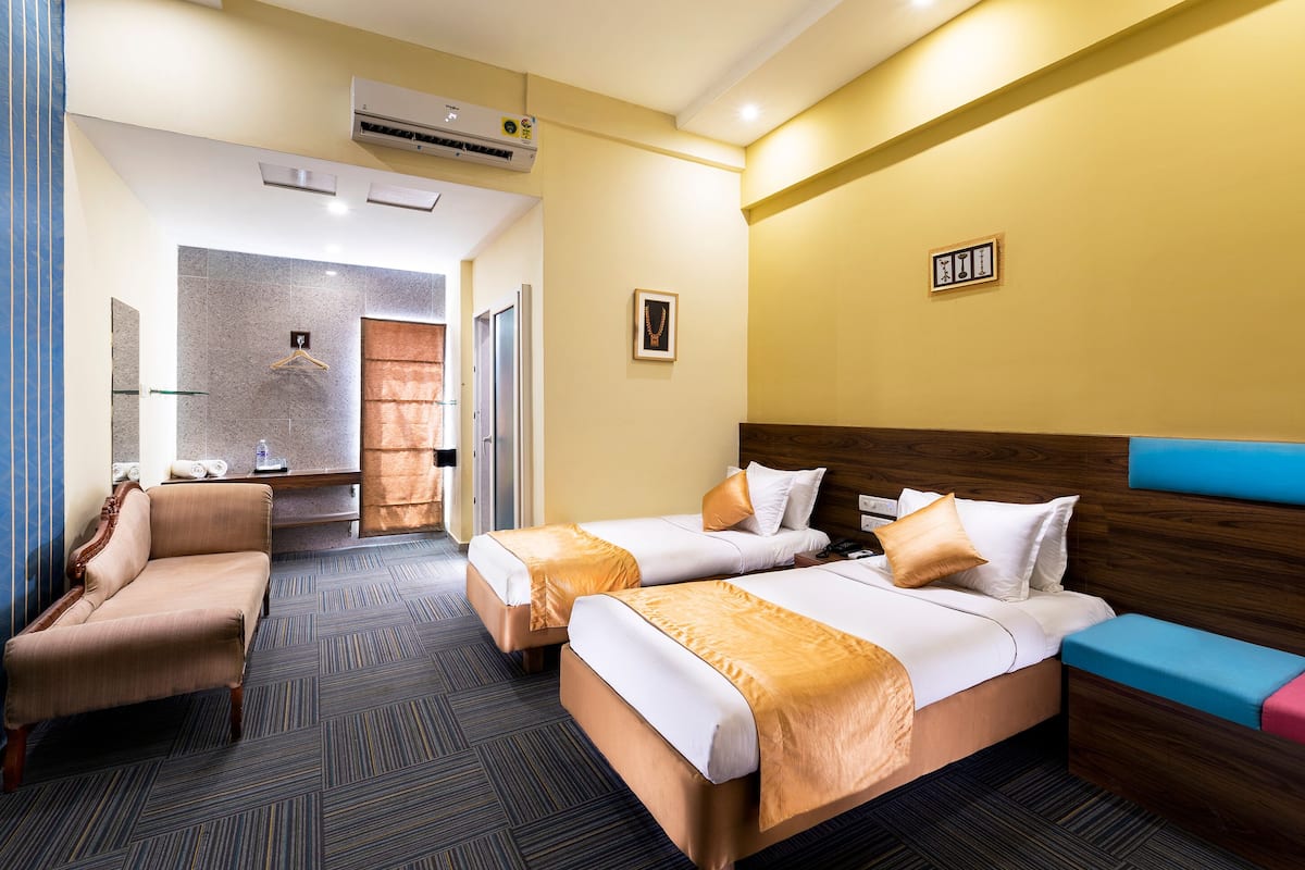 A hotel room with two beds, a sofa, a wooden headboard, and a small desk.