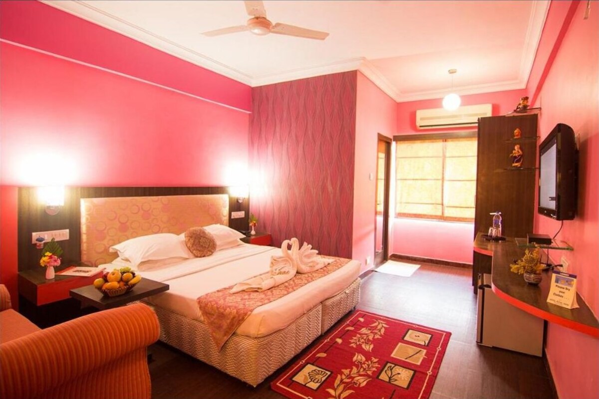 A hotel room with a bed, a desk, a chair, a television, and a reception desk.