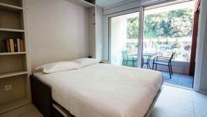 A bedroom with a bed, a bookshelf, and a view of a balcony with chairs. - Studio with balcony near the center of Locarno (YELLOW STUDIO 12) (Locarno)
